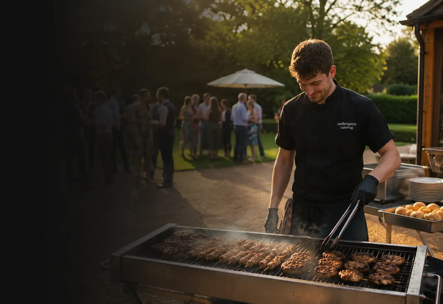 Chef turning burgers and sausages on an outdoor charcoal grill at an event