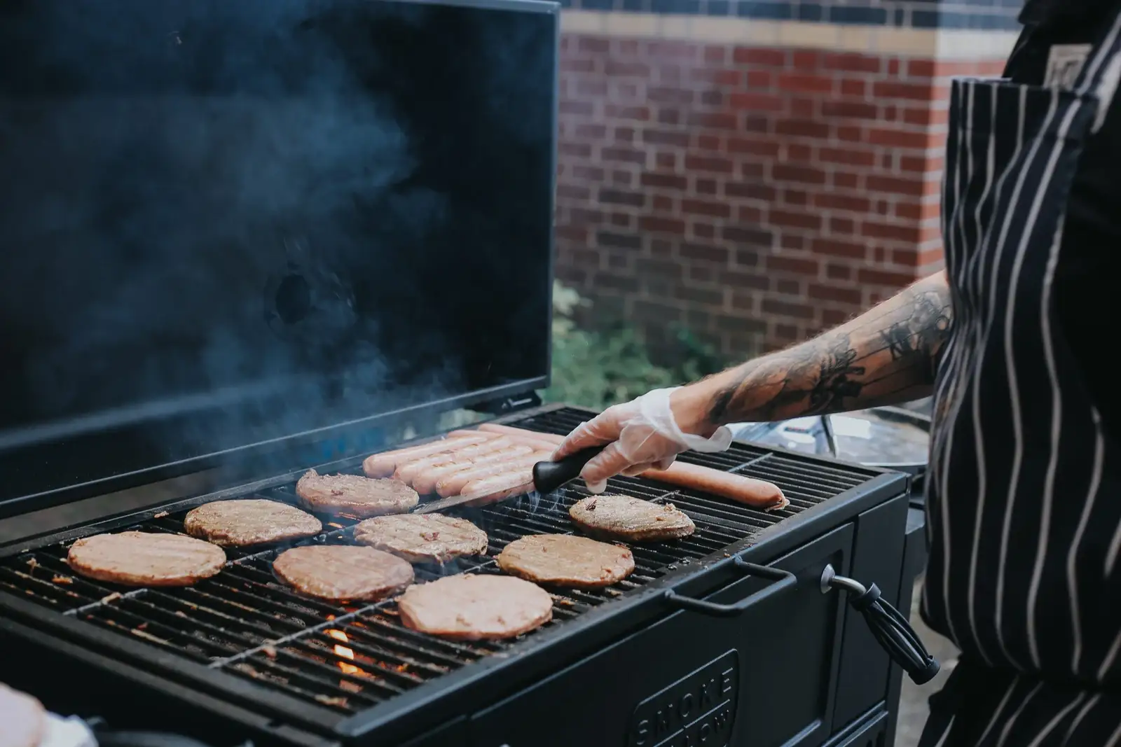 A party caterer wearing an apron cooking food on a barbeque