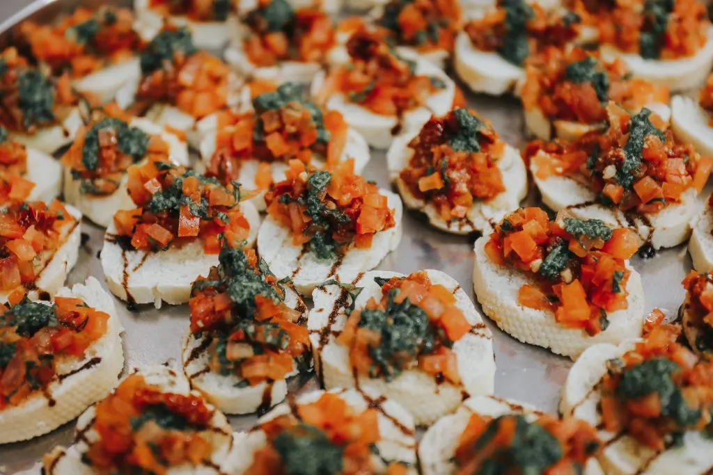 A tray of bruschetta topped with chopped tomato, pesto and a balsamic drizzle
