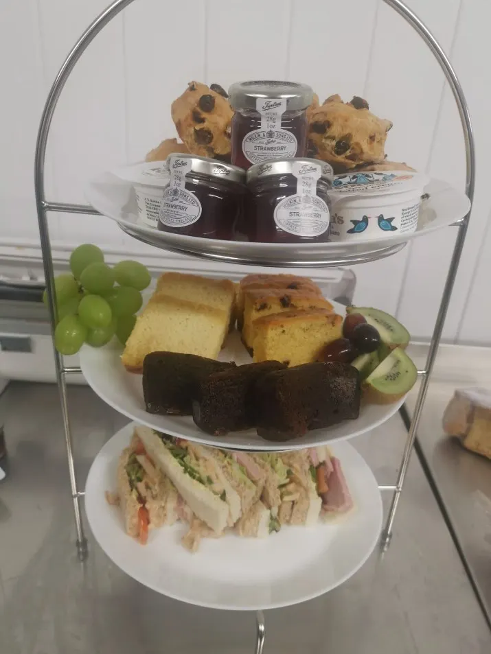 A three-tier afternoon tea stand with sandwiches, cake slices, fruit scones, jam and clotted cream