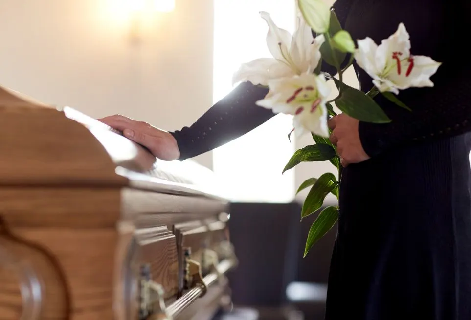 A woman laying flowers on a coffin of her loved one at their funeral which has been fully catered for.
