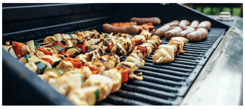 Chicken and vegetable skewers and sausages cooking on a barbecue grill