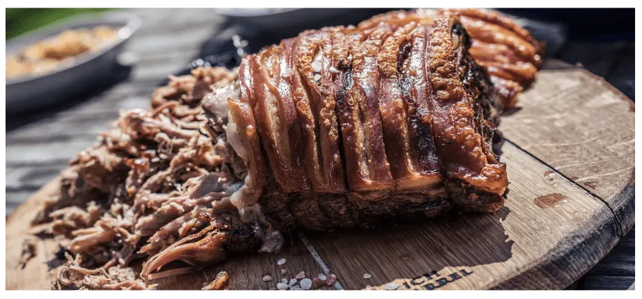 A joint of roast pork with crisp crackling on a wooden board, part of it already pulled