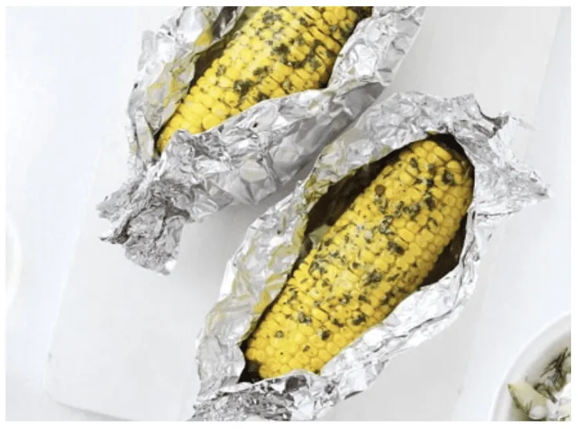 Two corn cobs in opened foil parcels, brushed with herb butter
