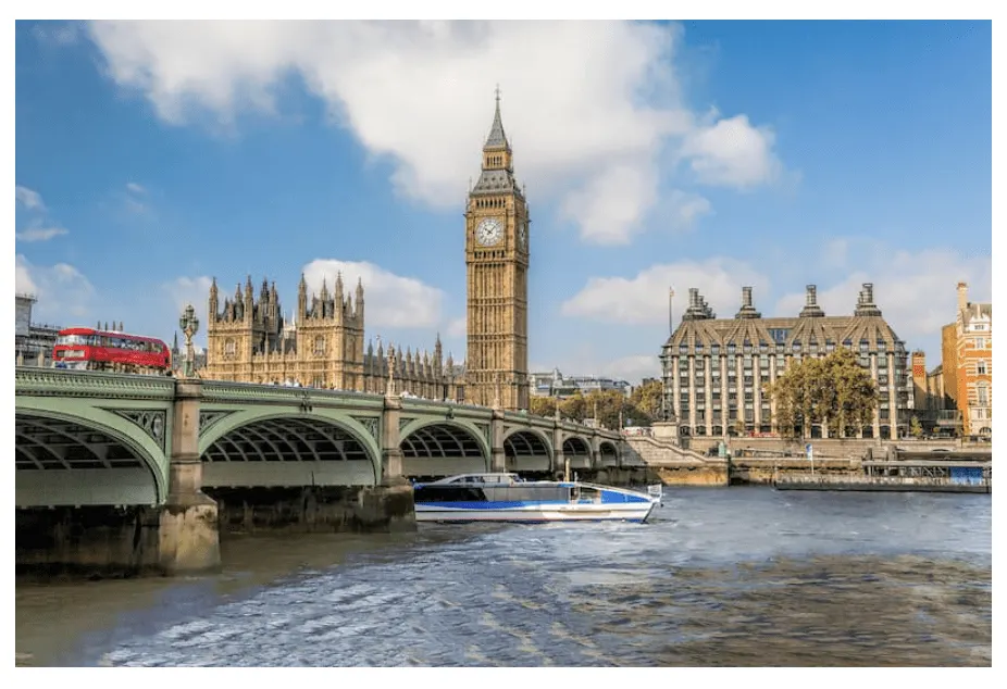 Big Ben and Westminster Bridge from the Thames, with a red bus crossing and a boat passing