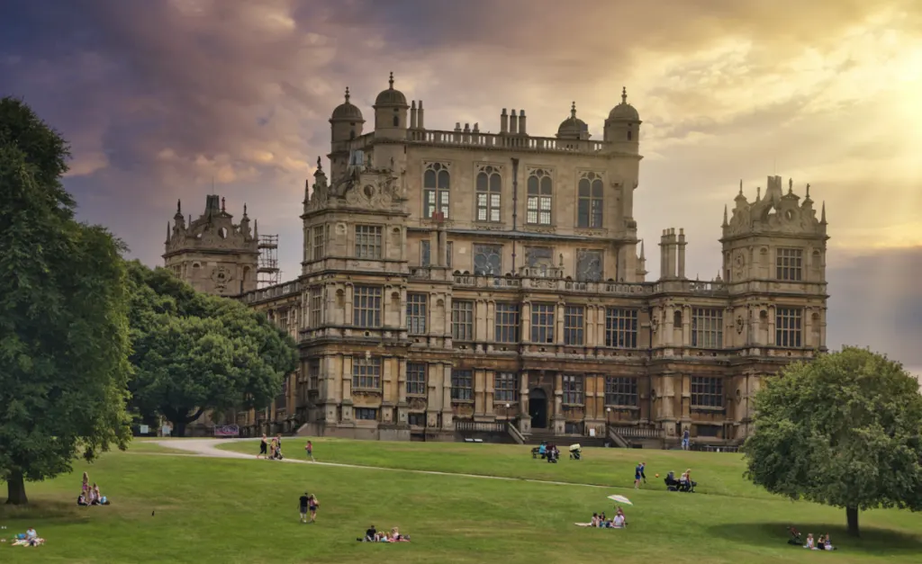 Wollaton Hall in Nottingham at sunset, with people sitting on the lawn in front of it