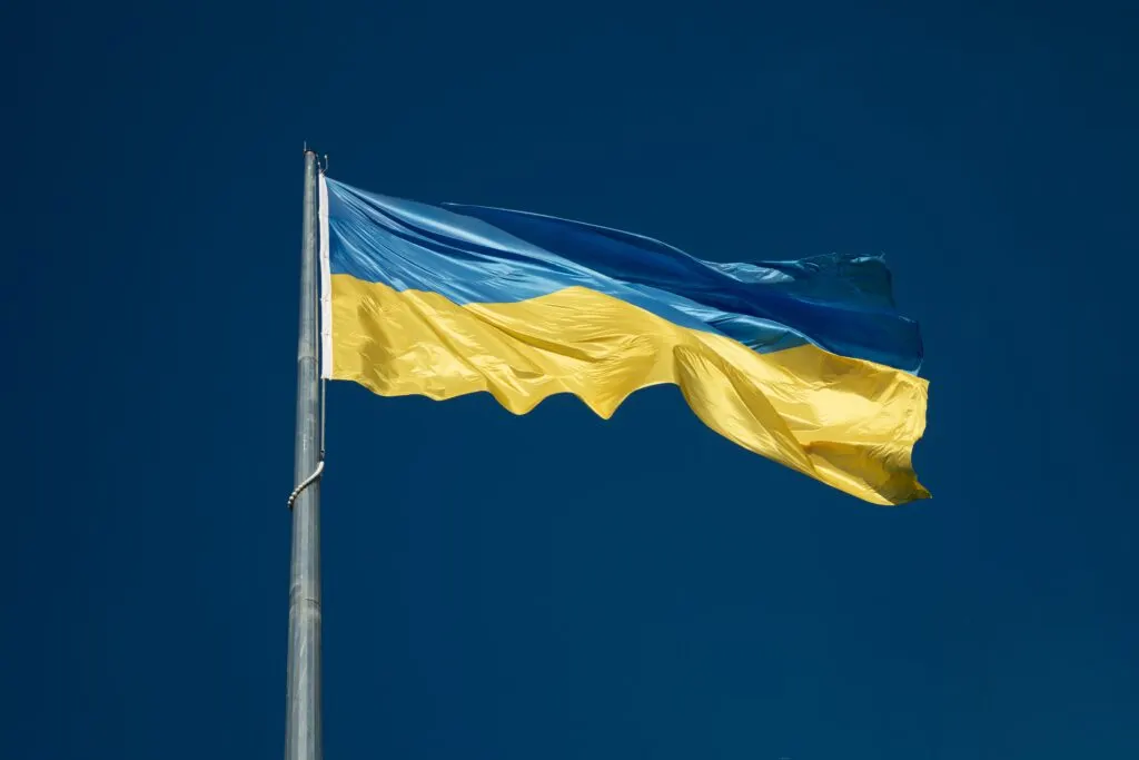 The flag of Ukraine flying from a mast against a deep blue sky